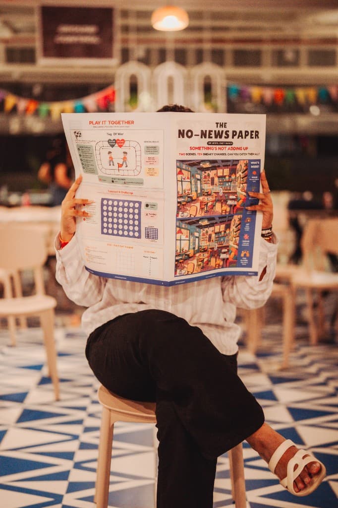 Someone holding open The No-News Paper Issue 3 at a café
